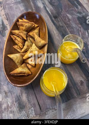 Samosas served with fresh mango juice on a wooden table, Lamu County, Lamu, Kenya Stock Photo