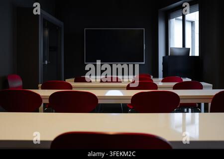 Empty modern classroom with red chairs and white desks facing blackboard Stock Photo