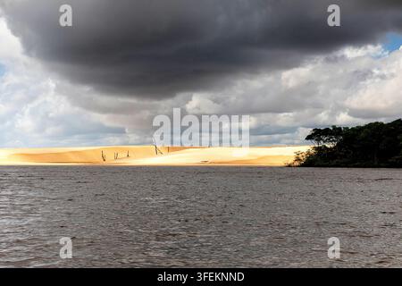 Eerie sun-bleached dead tree trunks standing among vast white sand dunes along the banks of the peaceful Preguicas River in Maranhao, Brazil. Stock Photo