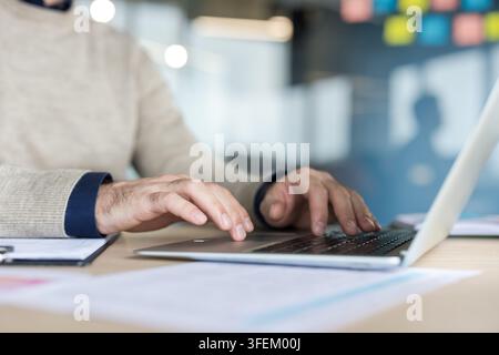Man's hands actively typing on a laptop keyboard at a desk, engaging in work, business communication, or creative writing in a modern office environment Stock Photo
