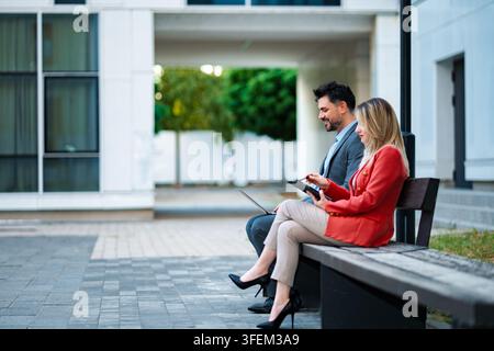 Business professionals collaborating outdoors using digital tablet and laptop Stock Photo