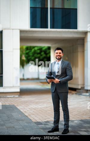 Confident businessman holding tablet standing in city corporate environment Stock Photo