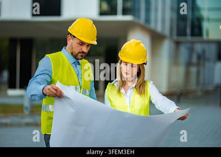 Engineers discussing blueprints planning construction project on site Stock Photo