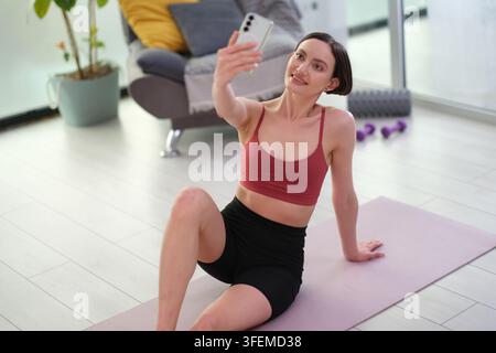 Pretty woman in activewear takes selfie by smartphone at home gym Stock Photo