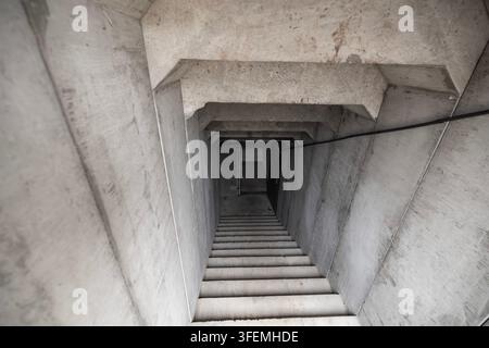 Concrete bunker entrance stairs leading down to a dark underground shelter with reinforced walls and heavy doors viewed from above Stock Photo