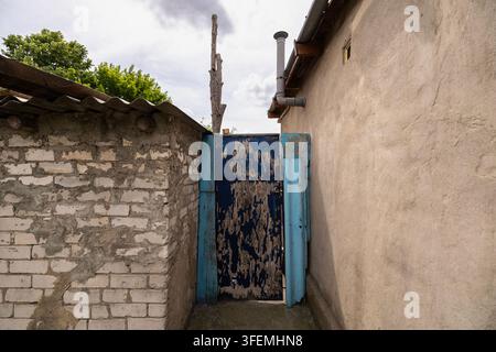 Old weathered blue wooden door between rustic buildings under a cloudy sky Stock Photo