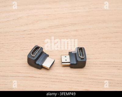 Right Angle HDMI Adapters on Wood - Two L-shaped HDMI adapters with gold-plated connectors are displayed on a light wooden surface, ready for electron Stock Photo