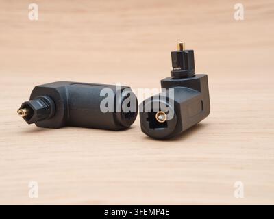 Two Black TOSLINK Optical Audio Adapters - Two L-shaped TOSLINK optical audio cable adapters are neatly displayed on a light wooden surface, ready for Stock Photo