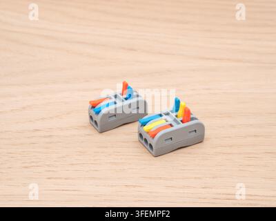 Electrical Wire Connectors on Wood - Two modern electrical wire connectors, featuring blue, orange, and yellow levers, are arranged on a light-colored Stock Photo
