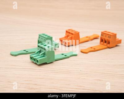 Electrical Connectors on Wooden Backgrou - Four colorful electrical connectors, two green and two orange, lay on a light-colored wooden surface, ready Stock Photo