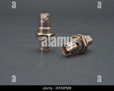 Two Metallic BNC Connectors - Two shiny silver BNC (Bayonet Neill-Concelman) connectors are displayed against a dark gray background, one standing upr Stock Photo