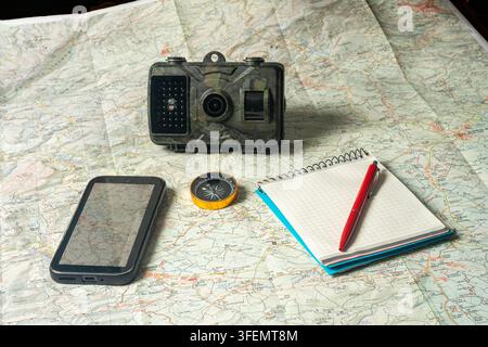 Trail camera, compass, smartphone and notebook on map for exploration Stock Photo