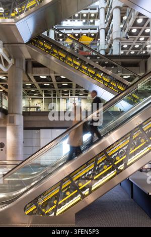 Commuters use escalators to navigate the Old Library, a landmark inside the iconic Lloyd's building in the City of London, UK. Stock Photo