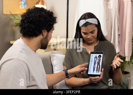 African team sitting in studio, holding tablet, pointing at fashion sketches near clothing rack Stock Photo