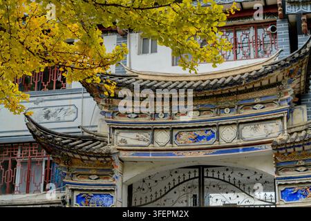 Ornate rooftop gateway framed by golden ginkgo branches, Dali Ancient Town Stock Photo
