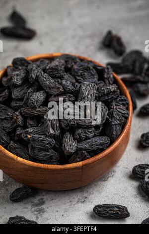 Black raisins in wooden bowl on stone background Stock Photo