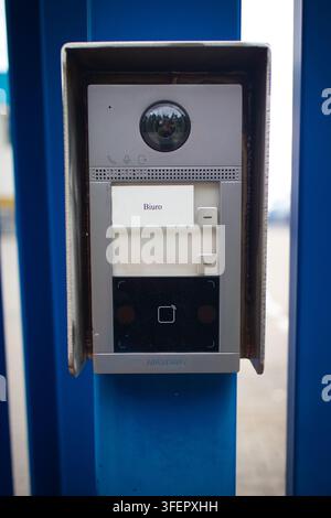 Modern video intercom mounted on blue pillar. Circular lens above label and button panel. Metal housing encases sleek, functional design. Ideal for se Stock Photo
