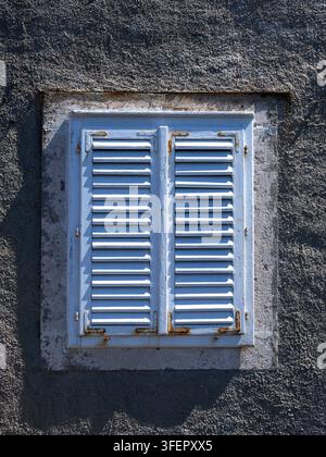 Old pale blue louvre vent on small window in stone wall for use as a background Stock Photo