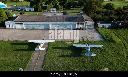 Aerial view of two small light aircraft parked on the grass in front of a large hangar at the Lisicji Potok airfield in Belgrade, City of Belgrade, Se Stock Photo