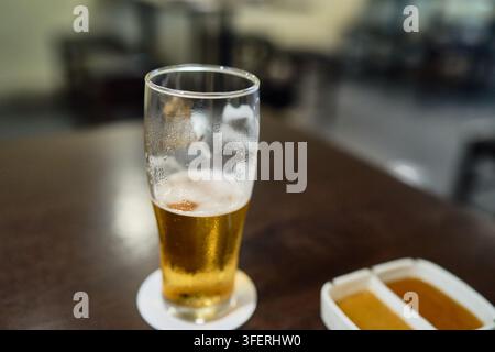 Half full glass of chilled lager beer with condensation resting on a coaster inside a bar. Stock Photo