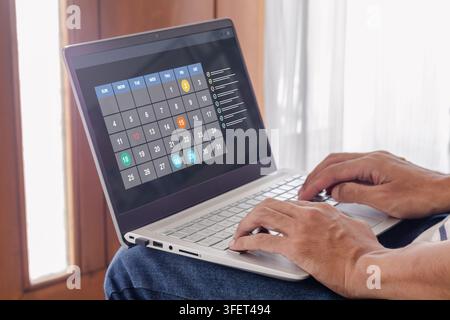 A person working on a laptop and using a digital calendar schedule Stock Photo