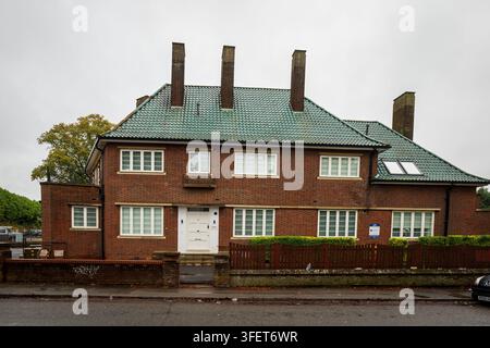 Two-storey brick residential house in Northampton with a distinctive green tiled roof, several tall chimneys, white-framed windows and a low wooden fe Stock Photo