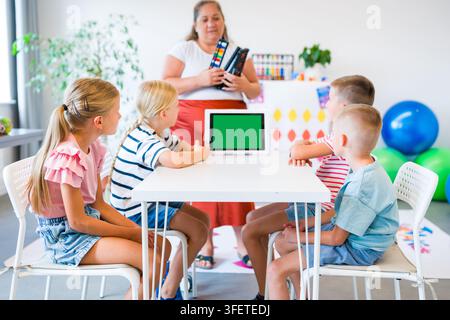 Teacher guides children practicing mental arithmetic and calculations with abacuses using a digital learning app during a classroom lesson. Stock Photo
