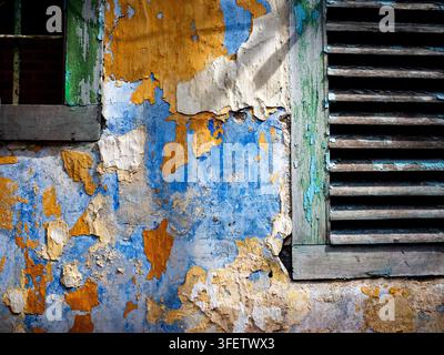 An old weathered concrete wall featuring cracked layers of blue and yellow peeling paint, distressed plaster, and rustic damaged texture Stock Photo