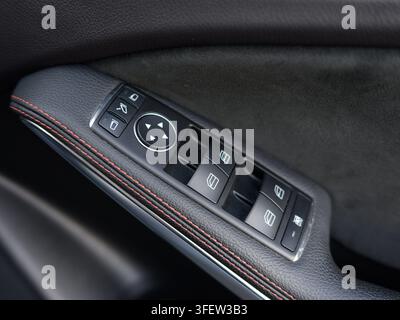 Close-up of a car door panel. Black control buttons feature window and mirror functions. Brown stitching accents the leather-like surface. Dark vehicl Stock Photo