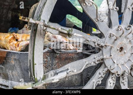 Whole lambs turn slowly on a metal spit behind an ornate wagon wheel, roasting over charcoal in a rustic outdoor setting and evoking traditional stree Stock Photo