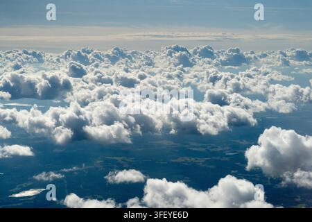 Aerial view over Swedish forests and lakes as fluffy white cumulus clouds form in the atmosphere, casting shadows on the landscape. Stock Photo