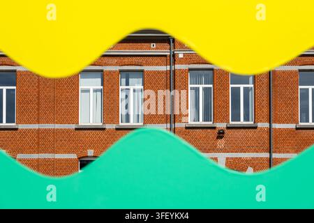 Red brick building facade with tall white windows, partly hidden by bold wavy yellow and turquoise shapes in a bright abstract architectural compositi Stock Photo
