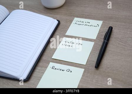 Professional workspace setup featuring yellow sticky notes with written tasks, a black pen, and an open lined notebook on a wooden desk. Stock Photo