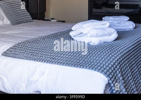 Fresh white towels neatly folded on prepared guest bedroom bed Stock Photo