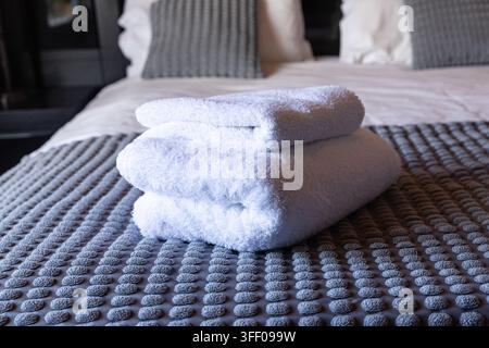 Fresh white towels neatly folded on prepared guest bedroom bed Stock Photo