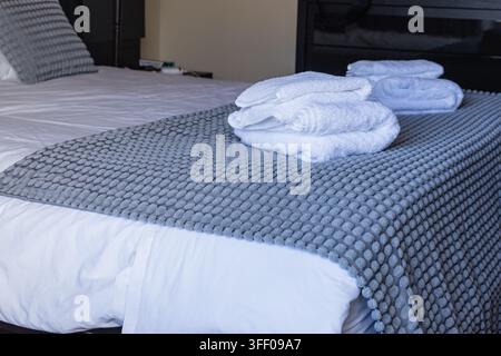 Fresh white towels neatly folded on prepared guest bedroom bed Stock Photo