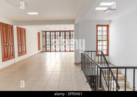 Empty Hallway with Stairs: A bright and airy hallway featuring tiled floors, wooden doors, and a staircase with a decorative railing leads Stock Photo
