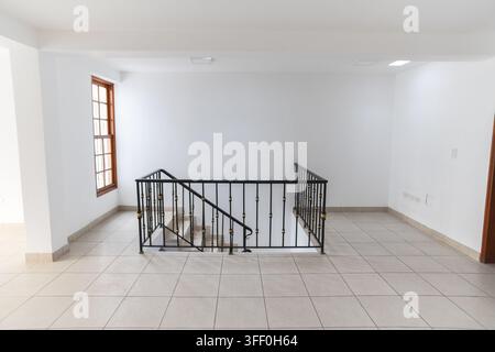 Empty House Interior with Staircase: A bright, empty interior of a house featuring a modern staircase with a metal railing, tiled floor Stock Photo