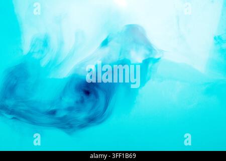 Abstract close-up of vibrant blue ink diffusing and swirling gracefully in clean water, creating soft smoke-like patterns against a light cyan backgro Stock Photo