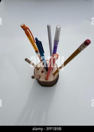 A rustic, handmade wooden log slice pencil holder filled with an assortment of colorful pens, pencils, and markers on a clean white background Stock Photo