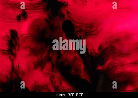 An abstract close-up of dark black ink dissolving and swirling in vibrant red liquid, creating fluid smoke-like patterns Stock Photo