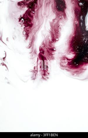 An abstract macro shot of deep red and maroon ink mixing and swirling in a white fluid, creating beautiful fluid patterns, bubbles, and textures with Stock Photo