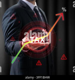 A businessman in a suit holds a futuristic hologram displaying the word TAX with rising percentage rates and warning symbols, representing inflation a Stock Photo