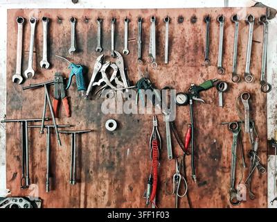 Assorted hand tools including wrenches and pliers hanging on a worn wooden board in an automotive garage or industrial workshop setting. Stock Photo