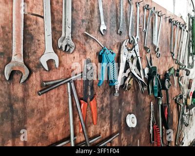 Collection of various mechanical hand tools including wrenches, pliers, and an air blow gun neatly organized on a weathered wooden tool board in an in Stock Photo