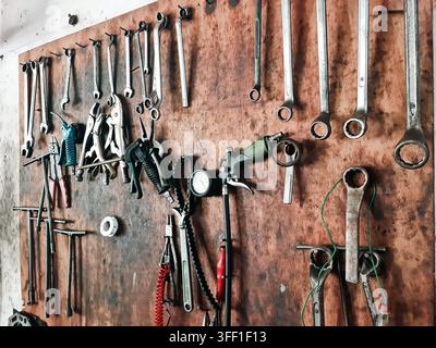 Assorted metal wrenches, pliers, and shop tools hanging on a rustic wooden board in a garage. Stock Photo