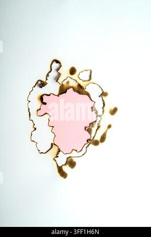 Abstract background of white paper with a charred, burnt hole revealing a pink inner layer. Useful for conceptual designs Stock Photo