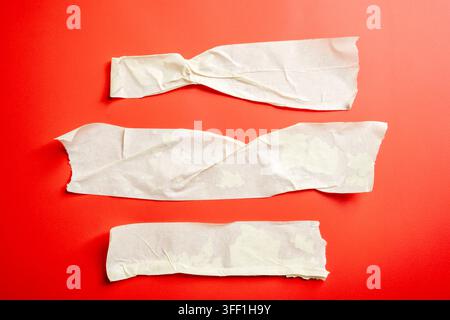 Three pieces of torn and crumpled white masking tape adhesive set on a vibrant red surface Stock Photo