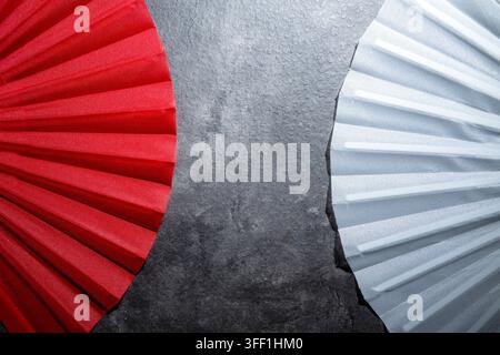 High angle close-up of a red fabric fan and a silver fabric fan positioned on a textured dark grey stone surface, creating a minimalist contrast Stock Photo