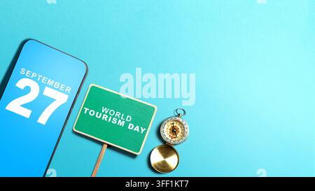 Flat lay of smartphone displaying September 27, a World Tourism Day sign, and a compass on a blue background with copy space Stock Photo
